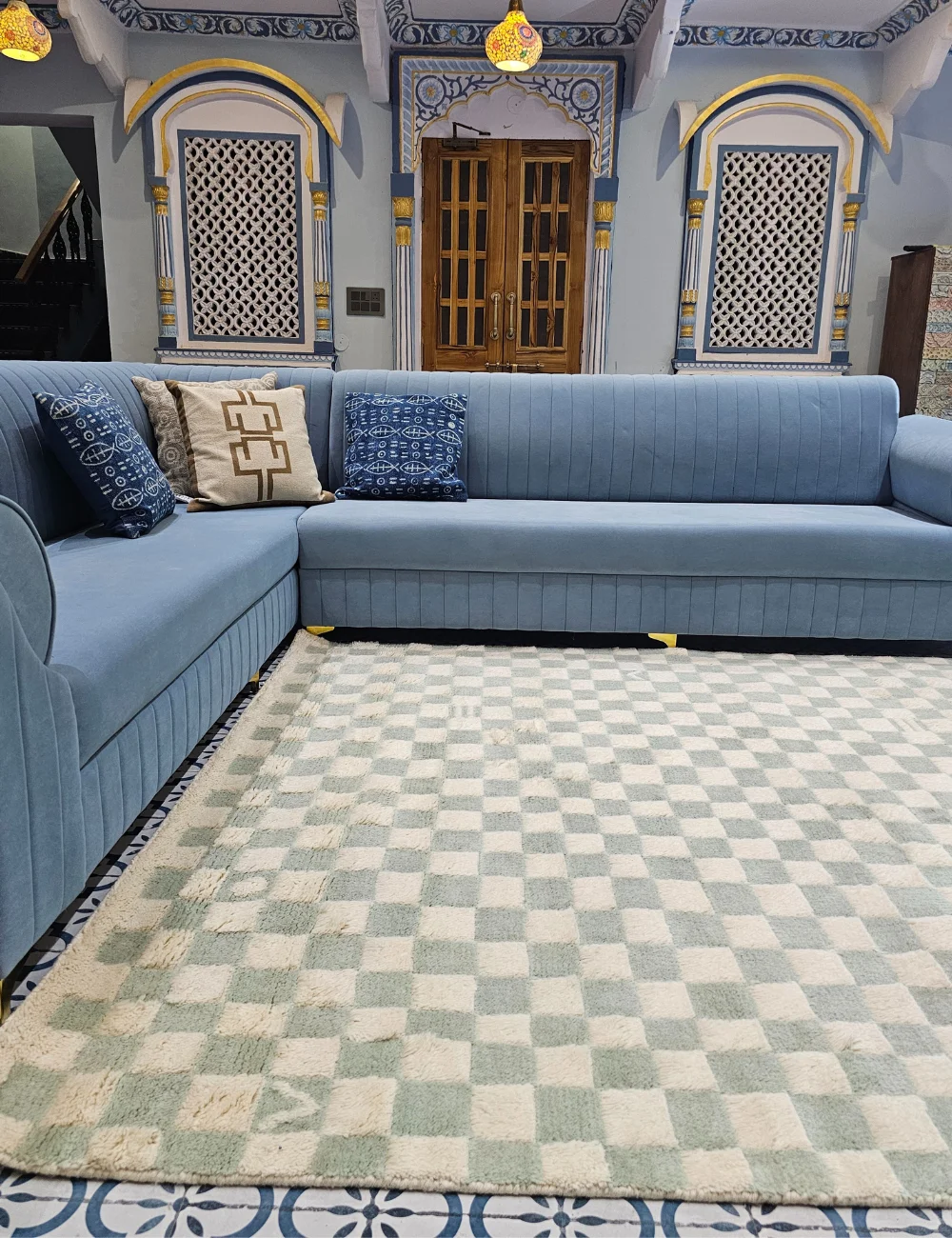 Green and white checkered rug in a luxurious living room with blue sofas and traditional Indian architecture.